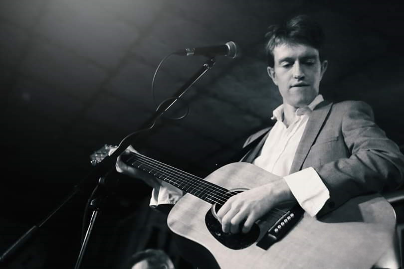 Jack Goodall playing a guitar in front of a microphone