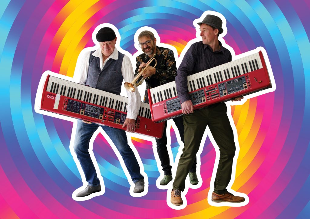 Richard Hughes and Phil Bond holding keyboards, with Oliver Carpenter stood in between them holding a trumpet, all three stood in front of a multicoloured whirl