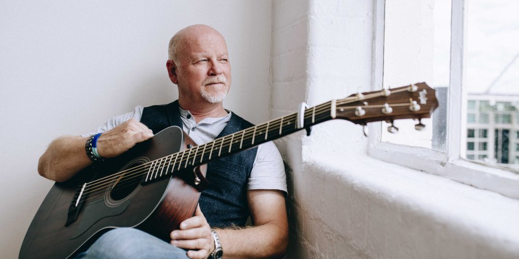 Joe Bayliss sat relaxing, looking out of a window with guitar propped up on his knee