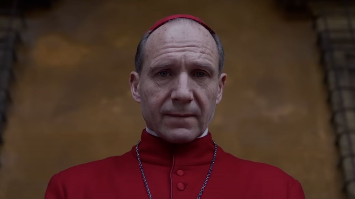 Ralph Fiennes as Cardinal Lawrence, wearing red vestments, looking towards the camera