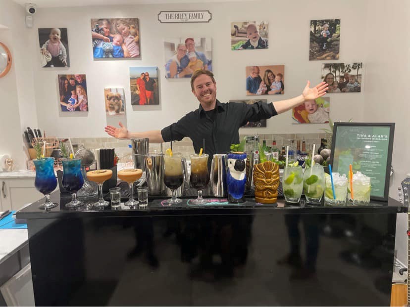 Lee Cowell wearing a black top behind a cocktail bar full on which there are some bottles