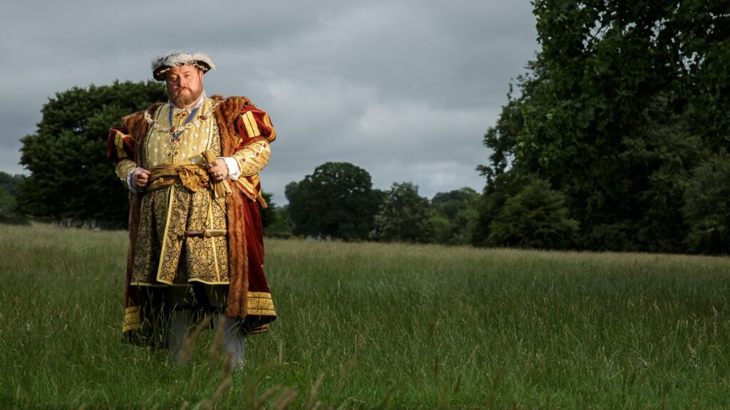 Jack Abbot dressed as King Henry VIII standing in a field, hands on hip