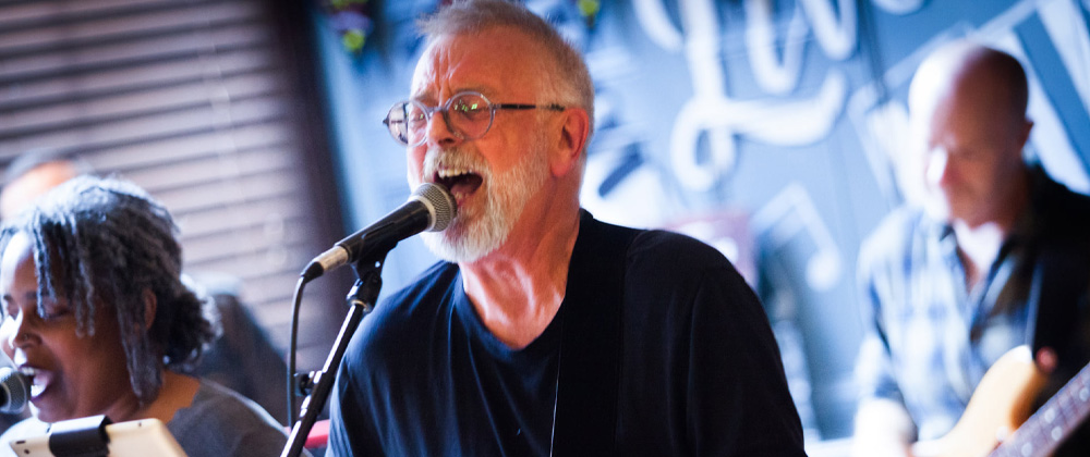 Pete Hyde of Pete Hyde & The Vieillards with white beard, wearing a black top and spectacles, singing into a microphone