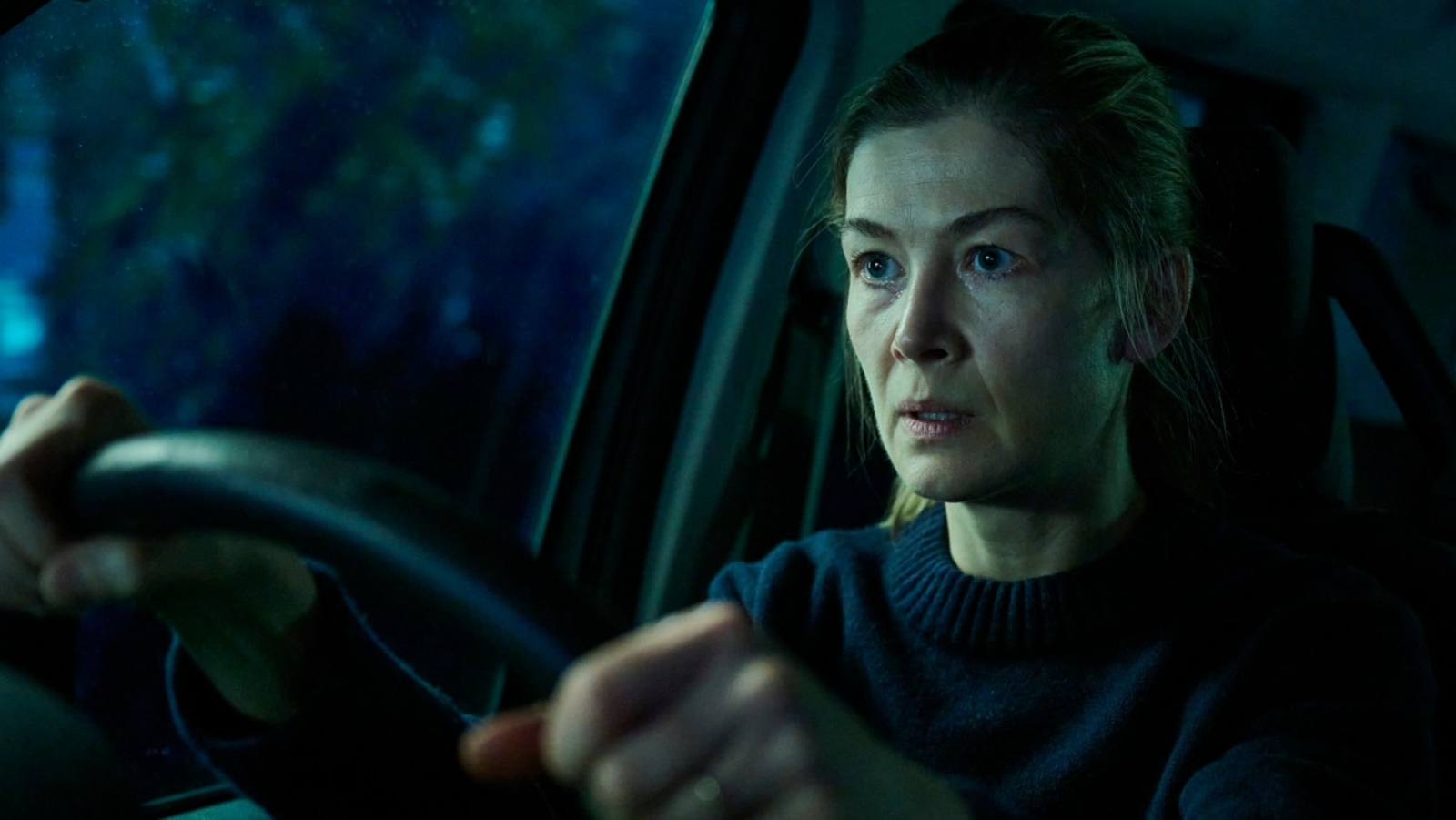 Hallow Road - Bromsgrove Arts Rosamund Pike as Maddie on Hallow Road, sat in vehicle, gripping steering wheel, wearing a dark sweater