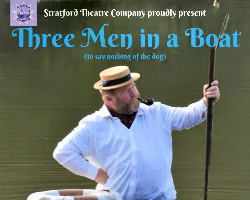Three Men in Boat - Giles Shenton as Jerome, standing in a river with a life buoy ring floating next him. Jerome is wearing a white shirt, black cravat, wearing a straw boaters hat, smoking a pipe, holding an oar and looking off into the distance
