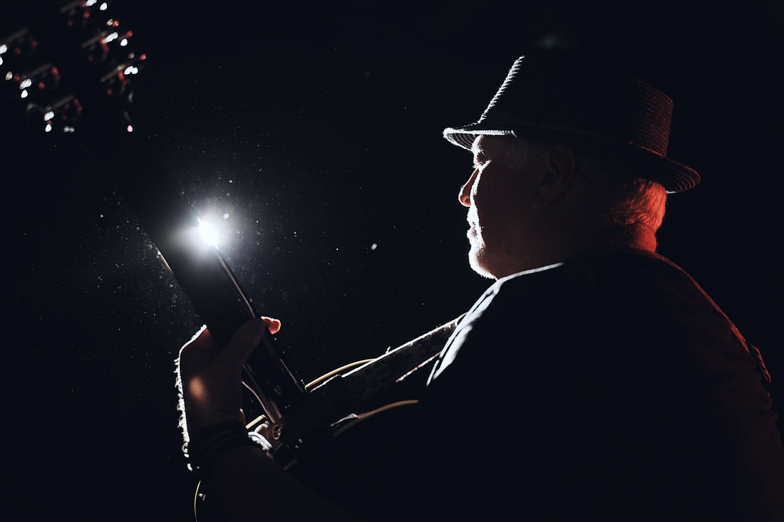 Silhouette of Gred Bartley wearing a hat and playing a guitar
