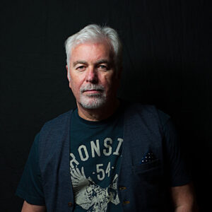 Gred Wilsom wearing a black t-shirt looking towards the camera, with grey hair & grey beard