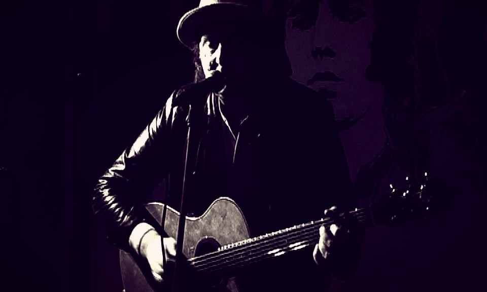 Tom Marin wearing a wide brimmed hat, playing a guitar