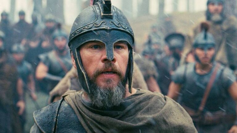 Matt Damon as Odysseus, looking forward with a greying beard and wearing a Grecian helmet, with an army behind him