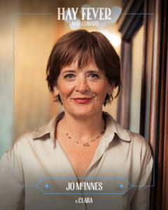 Portrait of a smiling woman with short brown hair in a beige blouse, presented as a poster for Hay Fever by Noël Coward, introducing the character Clara.